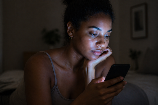 Young woman illuminated by phone screen at night, showing effects of blue light exposure on skin and digital aging