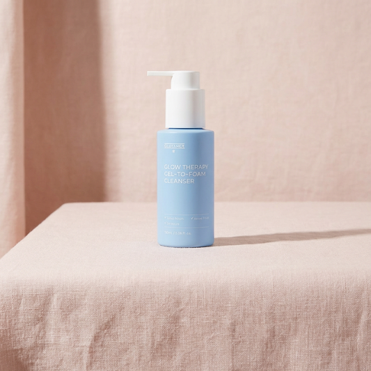 Blue bottle of Glutanex Glow Therapy Gel-To-Foam Cleanser on a beige surface with a soft pink background.